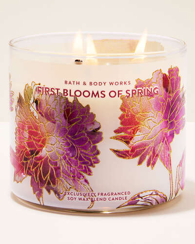 A lit three-wick candle in a glass jar with pink and purple flowers on it