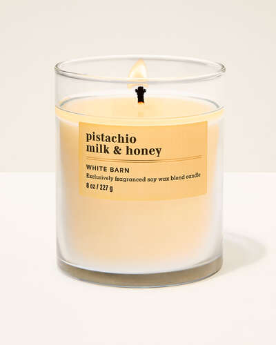 A white candle in a glass jar with a yellow label