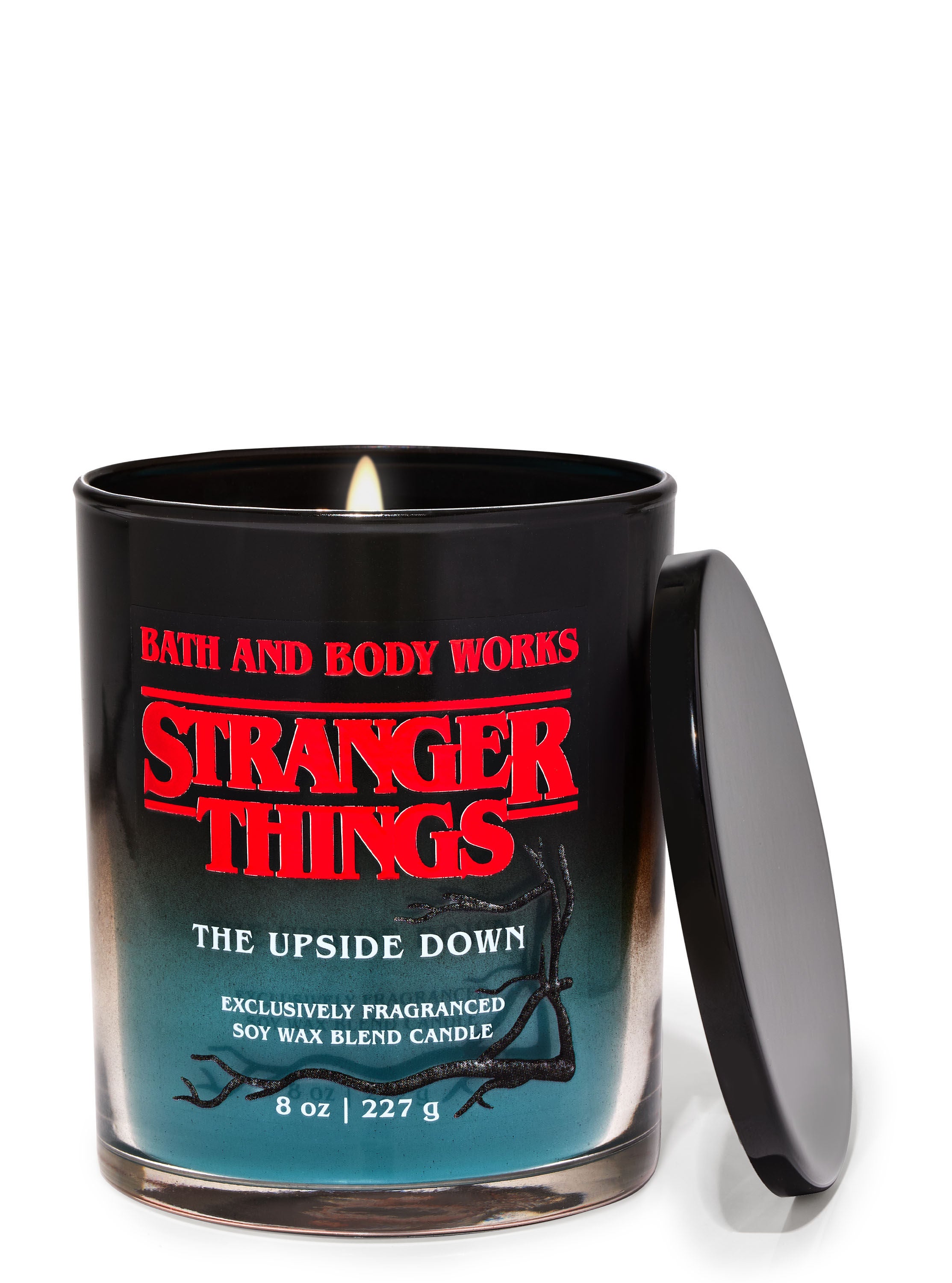 A black jar single wick candle with a black lid leaning on it